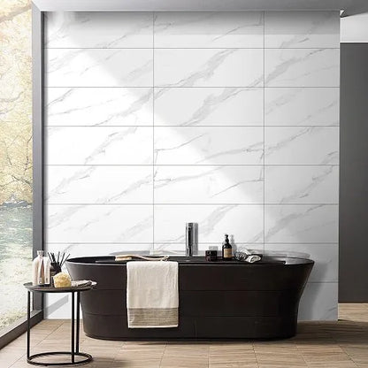 Large white marble-look wall tiles with soft gray veining, shown in a modern bathroom setting behind a black freestanding bathtub with a white towel draped over the side.