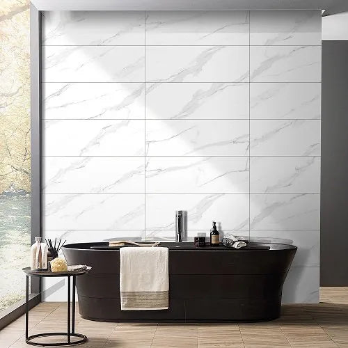 Large white marble-look wall tiles with soft gray veining, shown in a modern bathroom setting behind a black freestanding bathtub with a white towel draped over the side.